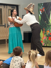 Characters from The Magical Pinata hold a clay pot in front of a young audience